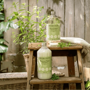Elegant French-style laundry scene featuring Durance Verbena Detergent and Softener nestled among fresh herbs and natural textures.