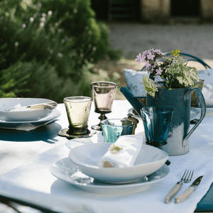 Outdoor table setting with white Bee Pasta Bowls, plates, colorful glasses, and a teapot on a white tablecloth.