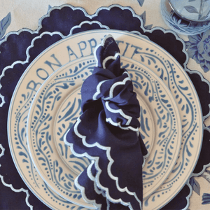 Decorative plate with 'Bon Appetit' text and a blue napkin on a matching tablecloth. Versailles napkins styled with matching placemats for a coordinated French table