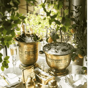 Gold Portofino ice buckets with champagne and fruit on a table with greenery.