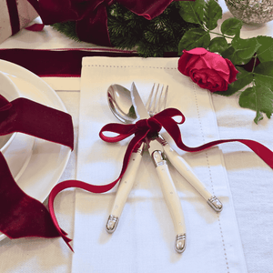 Laguiole cutlery set with red ribbon on a white linen tablecloth with flowers and ribbons.