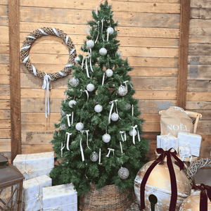 Decorated Christmas tree with ornaments, Oversized gold Christmas bells with red velvet ribbons and presents against a wooden wall. Handwoven Christmas tree skirt.