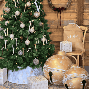 Decorated Christmas tree with ornaments, presents, and large gold bells against a wooden wall. Metal Christmas tree skirt.