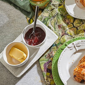 A stoneware condiment set with dragonfly motifs, including two bowls and a plate, presented on a table with breakfast items.