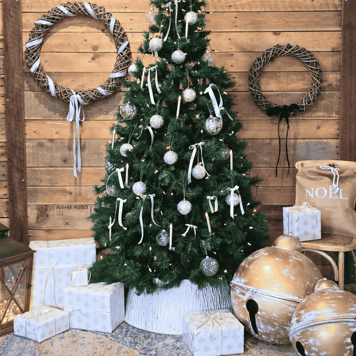Decorated Christmas tree with oversized Christmas bells and wreaths on a wooden wall.