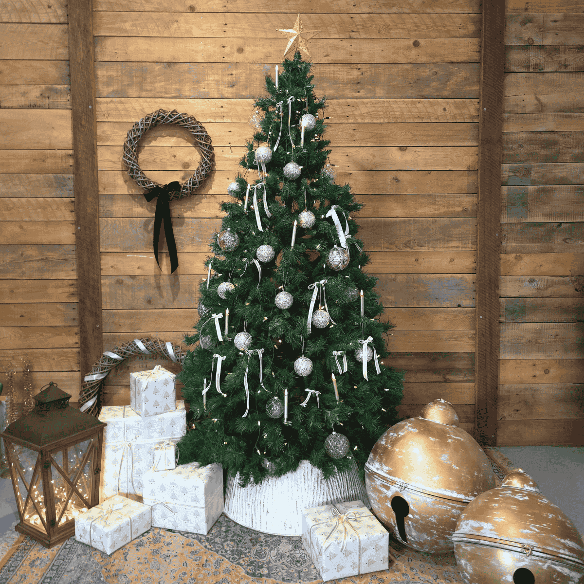 Decorated Christmas tree with ornaments and presents against a wooden wall.  Oversized gold Christmas bells  – Malmaison Noël décor