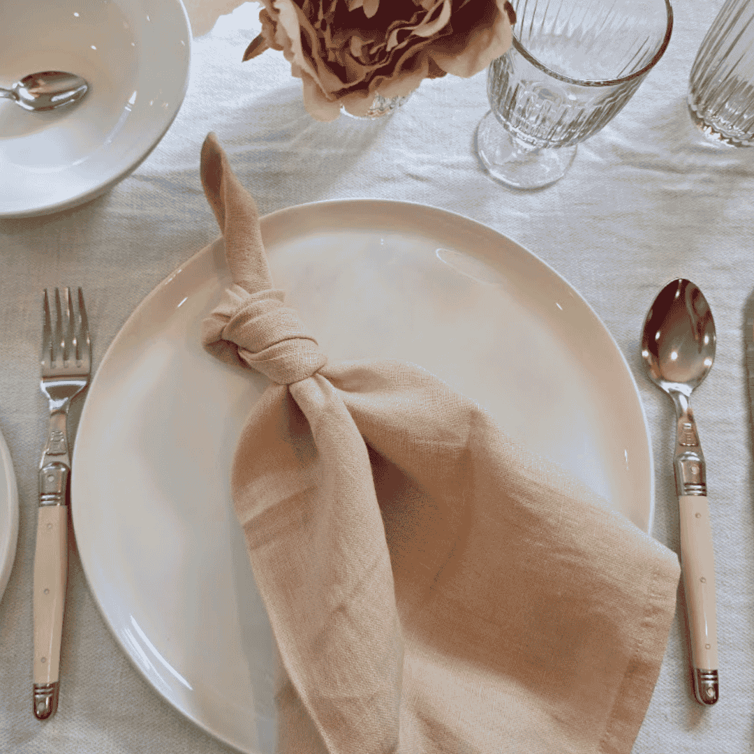 Blush linen napkin styled on white ceramic plate with simple table setting with Laguiole