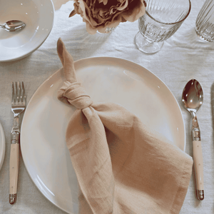 Blush linen napkin styled on white ceramic plate with simple table setting with Laguiole