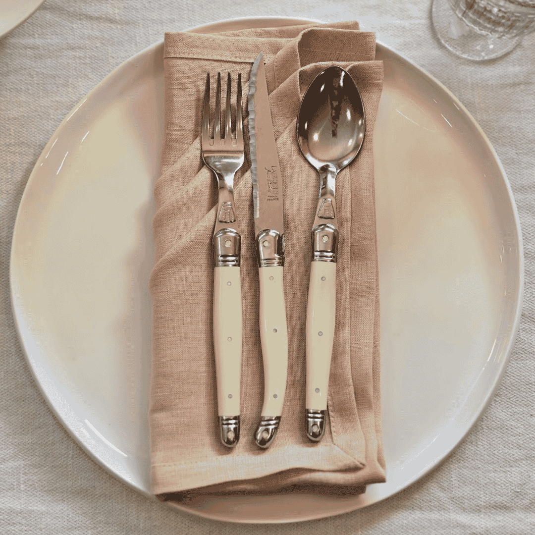 Blush linen napkin styled on white ceramic plate with simple table setting with Laguiole cutlery