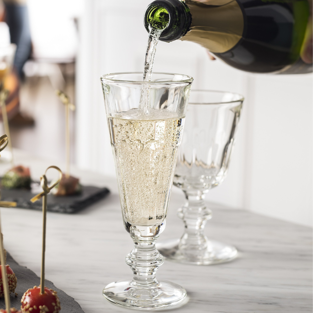 Champagne being poured into a La Rochere Champagne glass on a table with wint glass and appetizers.