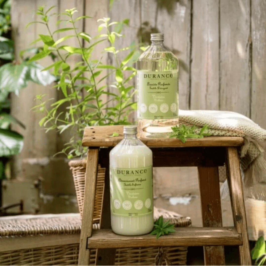 Elegant French-style laundry scene featuring Durance Verbena Detergent and Softener nestled among fresh herbs and natural textures.