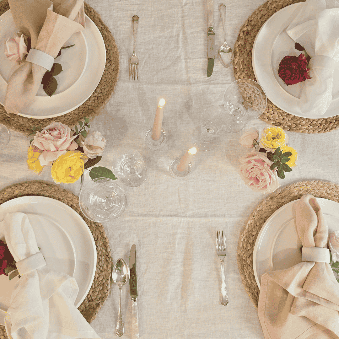 Elegant table setting with plates, napkins, flowers, and candles on a light surface.
