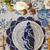 Decorative table setting with a blue and white plate, napkin, and cutlery on a floral tablecloth.  Malmaison - Luxe & Beau - Versailles Embroidery Heirloom Placemats - Navy