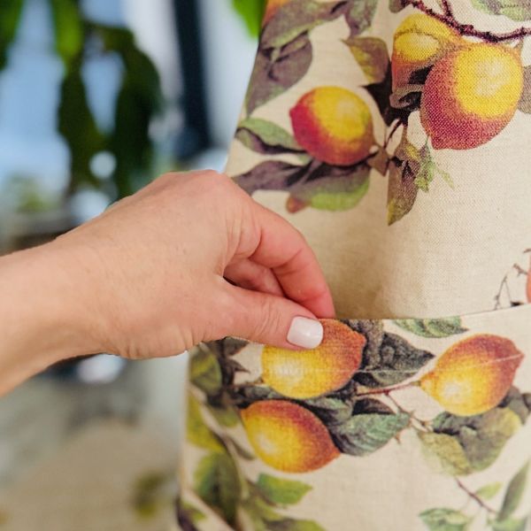 Woman in a lemon-patterned apron and straw hat picking lemons from a tree.  Menton lemon apron styled in a French countryside.