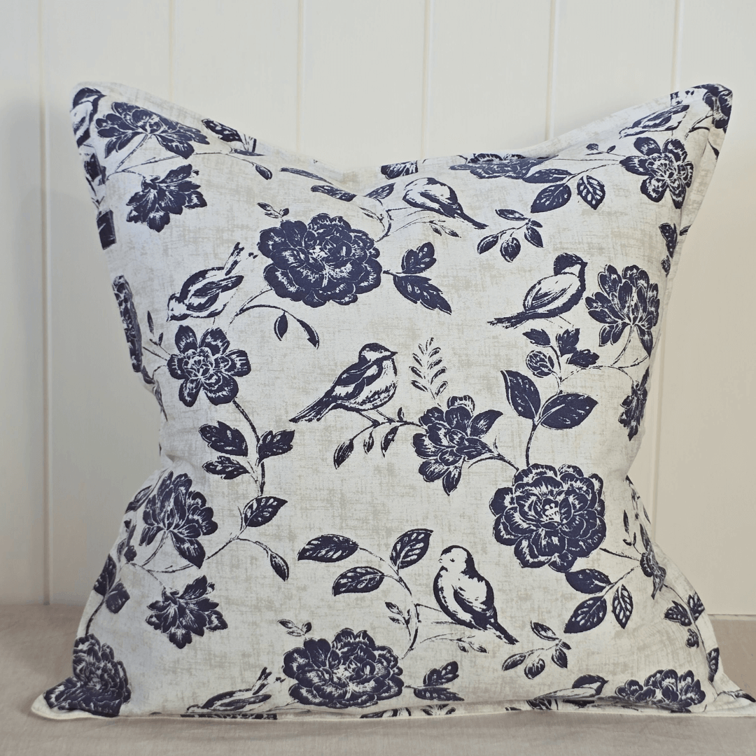 Decorative square cushion with floral and bird pattern on a neutral background and orchid in pot
