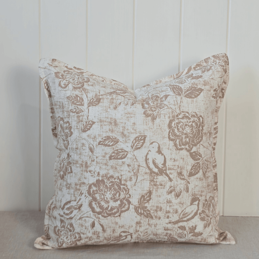 Decorative linen square cushion with floral and bird pattern next to a potted orchid on a neutral background