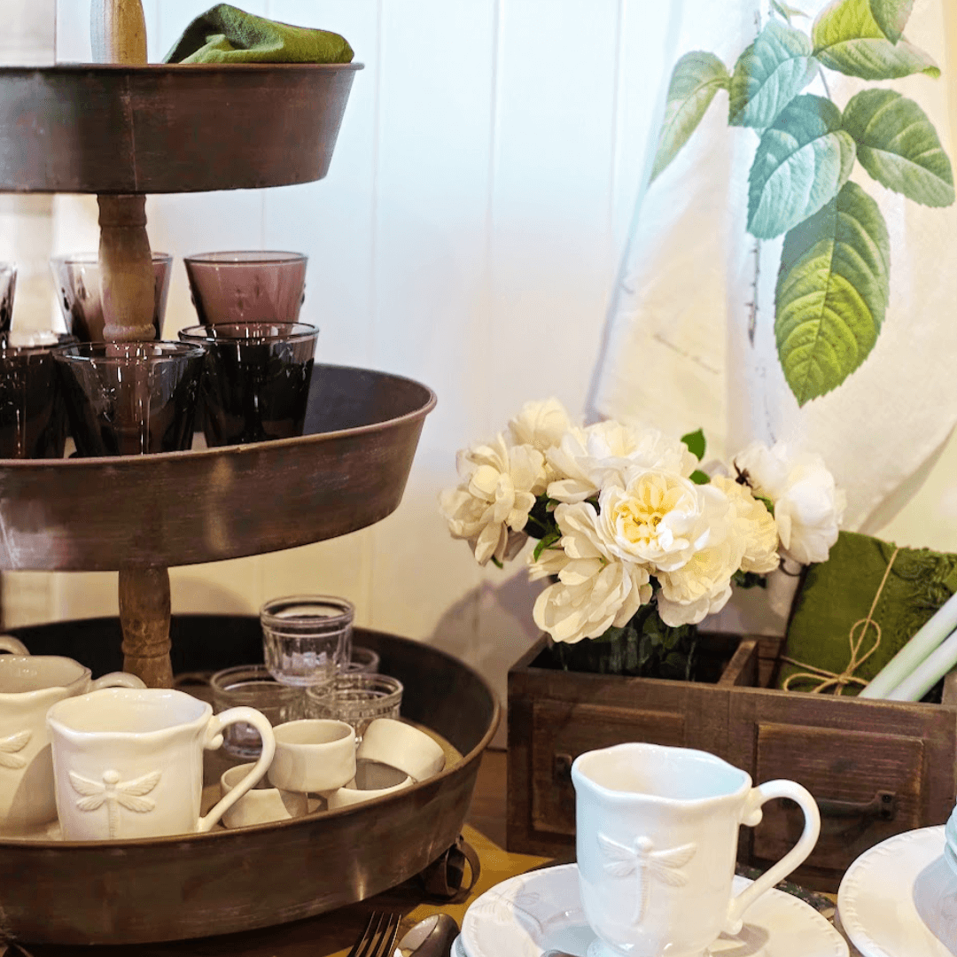 French Country Three-tiered metal tray with cups and saucers, white flowers in a wooden box, and a Redoute Tea Towel with leaf pattern.