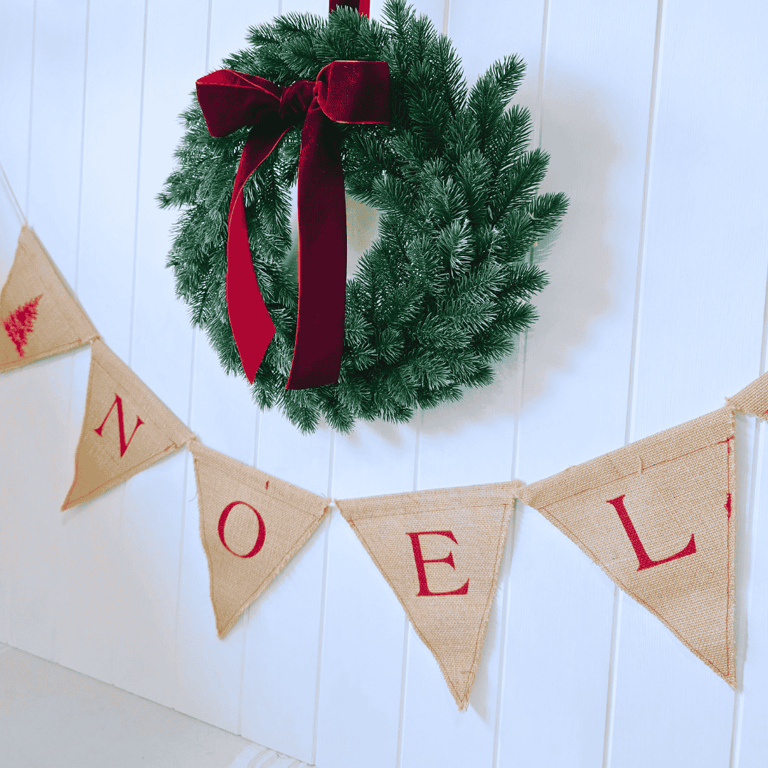 Christmas wreath with red ribbon and 'NOEL' banner on a white wooden background