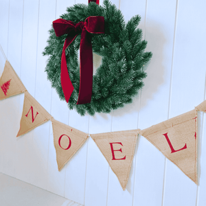 Christmas wreath with red ribbon and 'NOEL' banner on a white wooden background