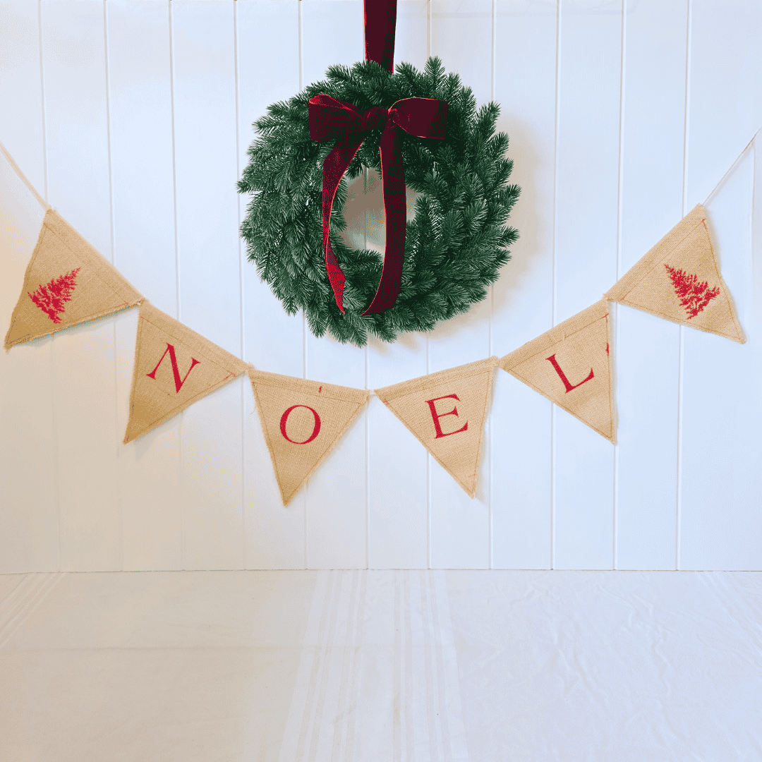 Christmas wreath with a red ribbon and 'NOEL' banner on a white wooden background