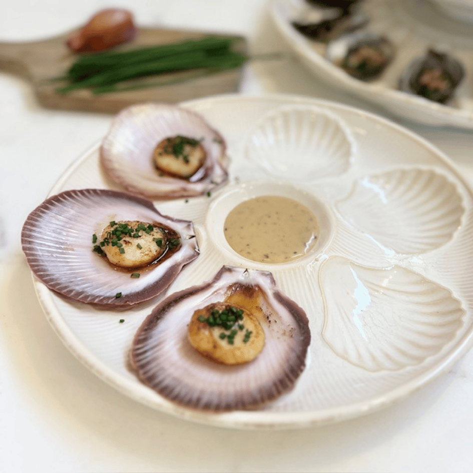 Scallops on a decorative Bessin Scallop Plate dish with a sauce in the center.