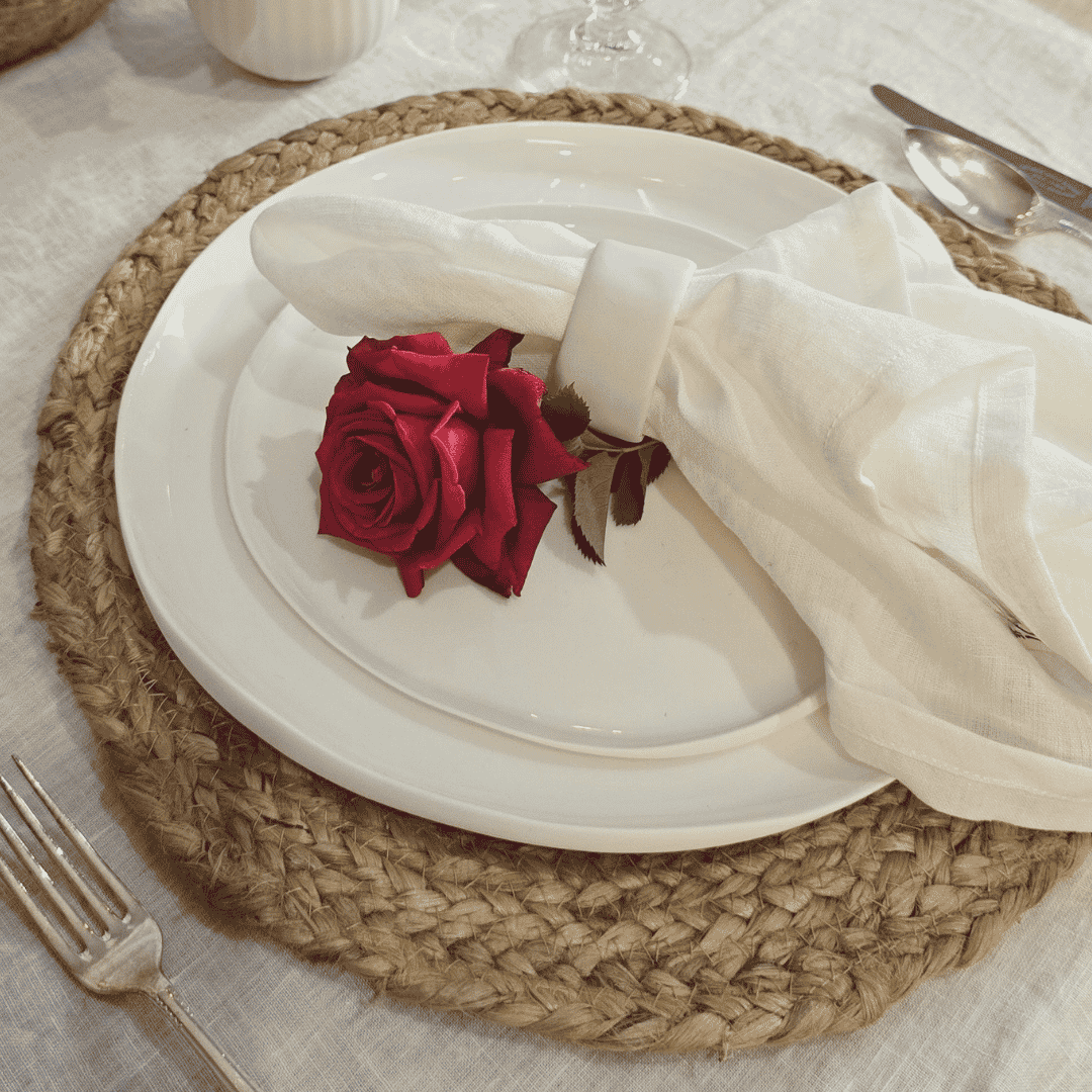 French Flax Napkin White - Place setting with a red rose on a white plate, surrounded by cutlery and a woven placemat.