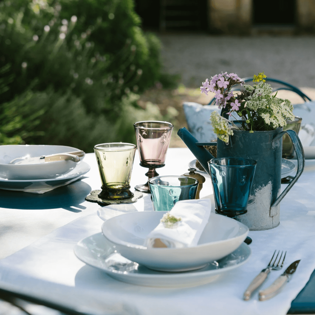 Outdoor table setting with white Bee Pasta Bowls, plates, colorful glasses, and a teapot on a white tablecloth.