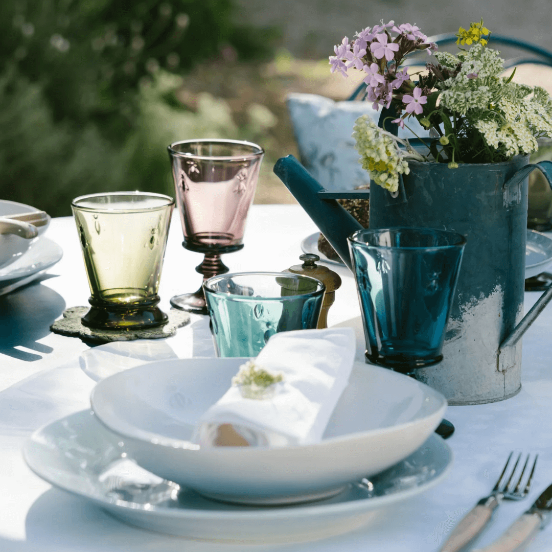 Closeup of White Bee Pasta Bowl and Blue Bee Dinnerplate.  French cutlery and La Rocher Bee Coloured Glasses.