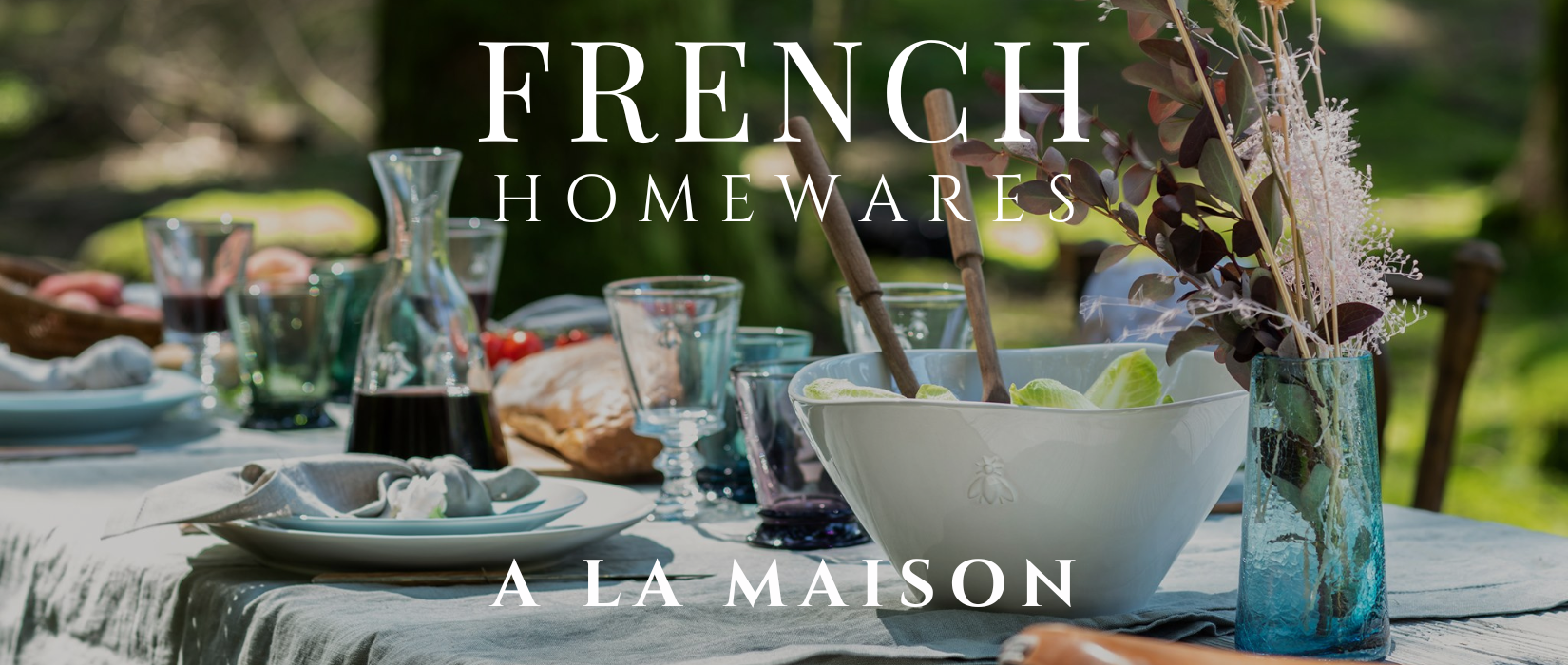 Table setting with glasses, bowls, and a bottle on a tablecloth with 'French Homewares A La Maison' text.