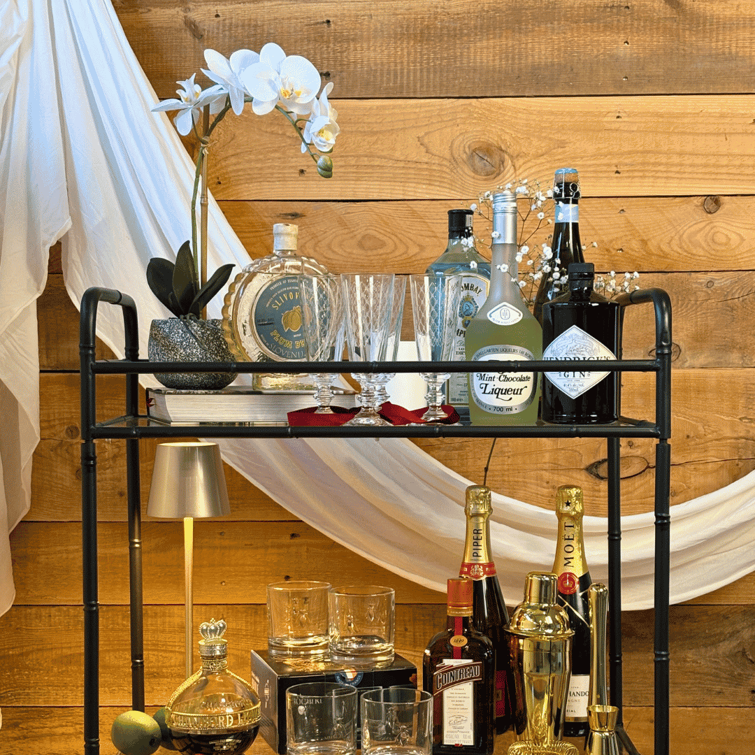 Bar cart with various bottles and glasses against a wooden wall.