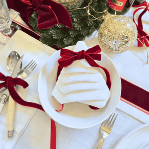 Christmas-themed table setting with red bows, gold ornaments, and white plates.  White napkin folded as christmas tree