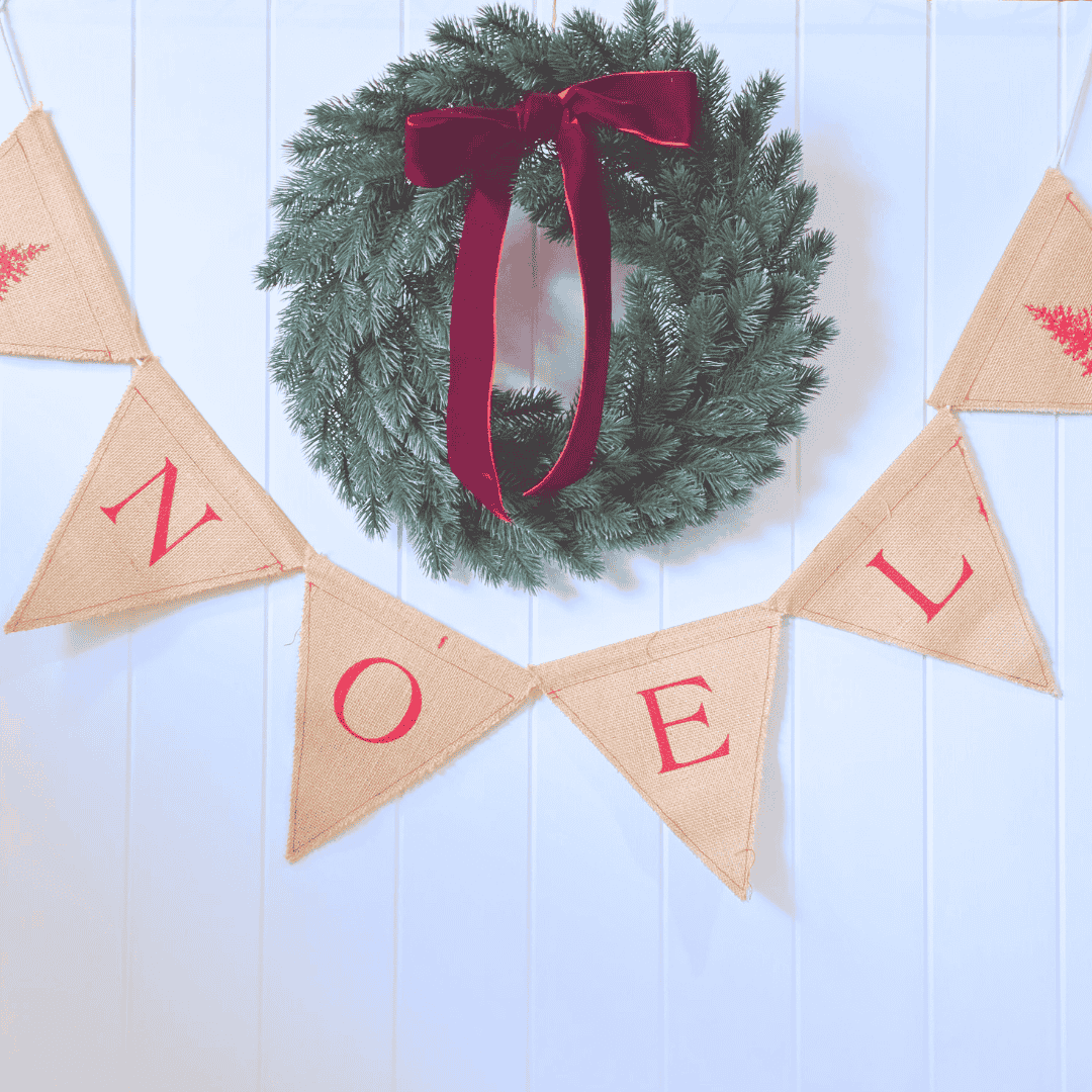 Christmas wreath with red ribbon and 'NOEL' banner on a white wooden background