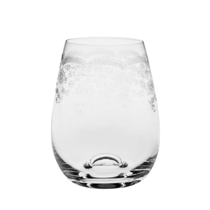 A stemless wine glass with floral etched patterns, containing a beverage and ice cubes, on a striped tablecloth.