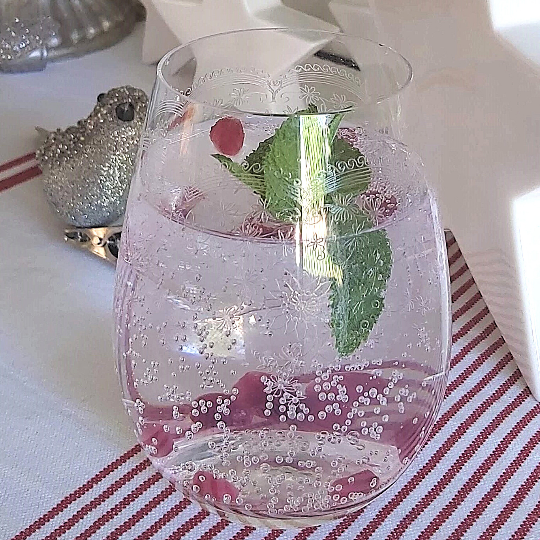 A stemless wine glass with floral etched patterns, containing a beverage and ice cubes, on a striped tablecloth.