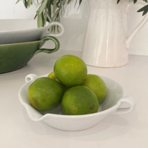 A small white ceramic Provence bowl on a kitchen bench, filled with green limes.