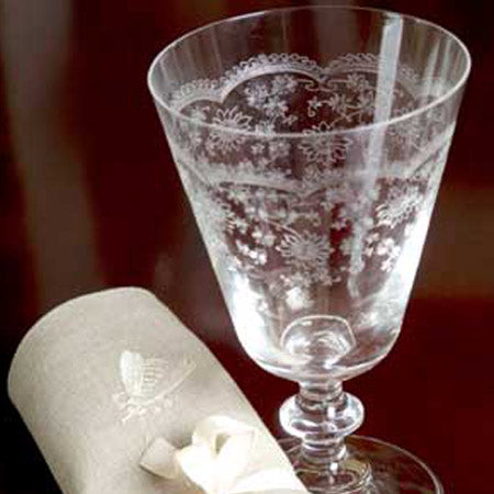 A clear crystal wine glass with etched floral patterns, displayed alongside a white cloth with an etched design.